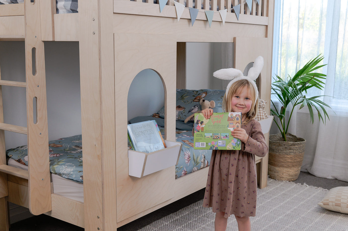 Child standing in a room with a wooden bunk bed and a plant.